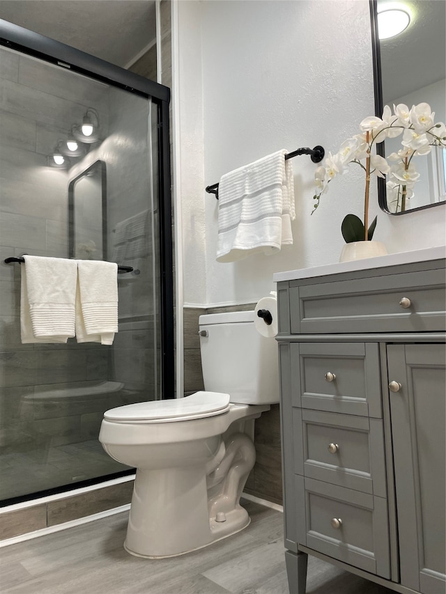 bathroom with vanity, hardwood / wood-style floors, a shower with shower door, and toilet