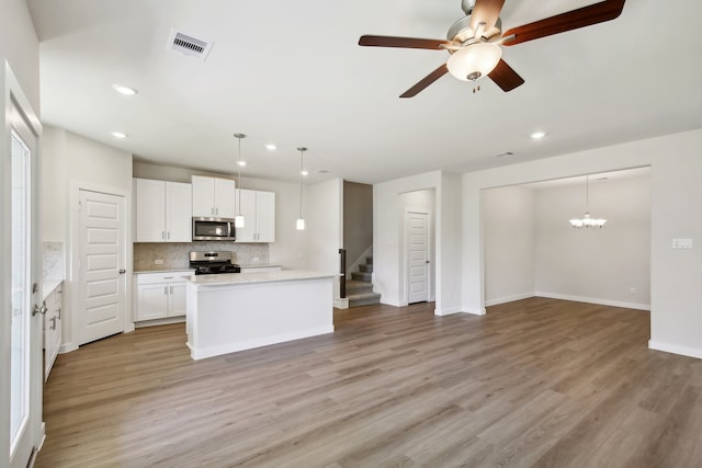 kitchen featuring light wood-type flooring, appliances with stainless steel finishes, tasteful backsplash, decorative light fixtures, and white cabinetry