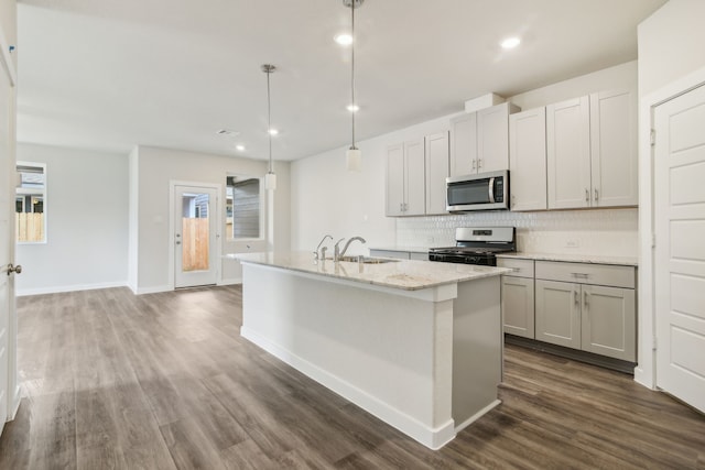 kitchen featuring sink, hanging light fixtures, stainless steel appliances, dark hardwood / wood-style flooring, and a center island with sink