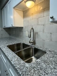 kitchen featuring light stone countertops, sink, decorative backsplash, and white cabinetry