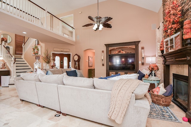 living area with arched walkways, high vaulted ceiling, a ceiling fan, stairs, and a glass covered fireplace