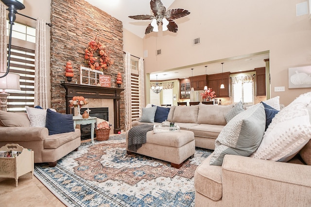 living area featuring ceiling fan with notable chandelier, a high ceiling, a fireplace, and visible vents