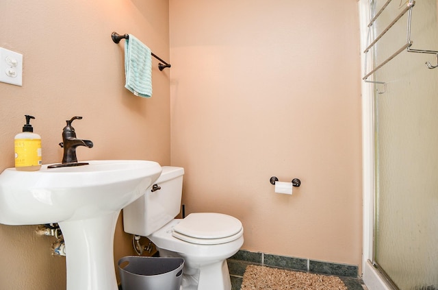 bathroom featuring toilet, a shower with door, and baseboards