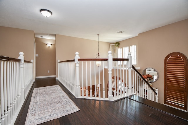 hallway featuring baseboards, visible vents, wood finished floors, and an upstairs landing