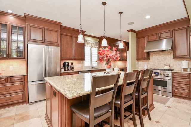 kitchen with appliances with stainless steel finishes, brown cabinets, a center island, under cabinet range hood, and a sink