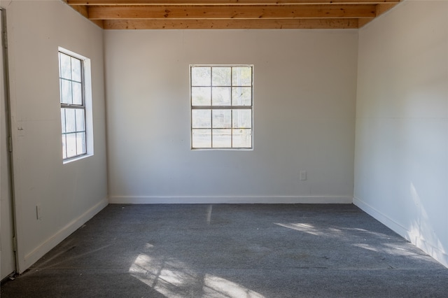 unfurnished room featuring plenty of natural light, beam ceiling, and dark carpet