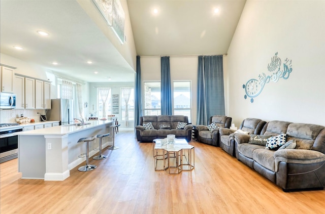 living room with light hardwood / wood-style floors, sink, and high vaulted ceiling