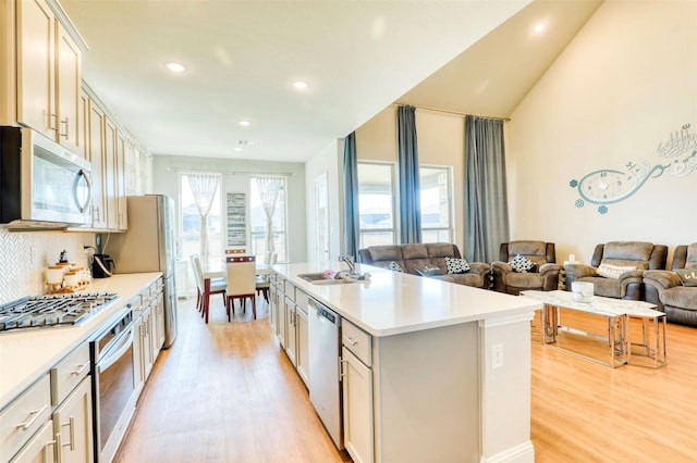 kitchen with backsplash, stainless steel appliances, sink, light hardwood / wood-style floors, and an island with sink