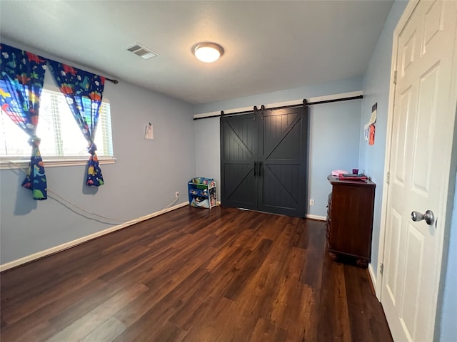 unfurnished bedroom with dark hardwood / wood-style floors and a barn door