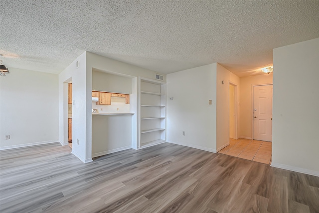 unfurnished living room featuring light hardwood / wood-style floors, a textured ceiling, and built in shelves