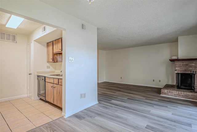 kitchen featuring a textured ceiling, stainless steel dishwasher, light hardwood / wood-style flooring, a skylight, and a fireplace