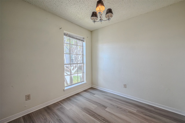 unfurnished room with an inviting chandelier, light hardwood / wood-style flooring, and a textured ceiling