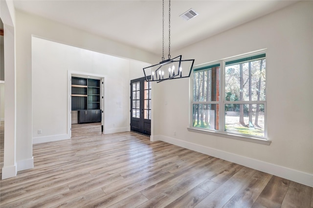 unfurnished dining area with french doors, light wood-type flooring, and a notable chandelier