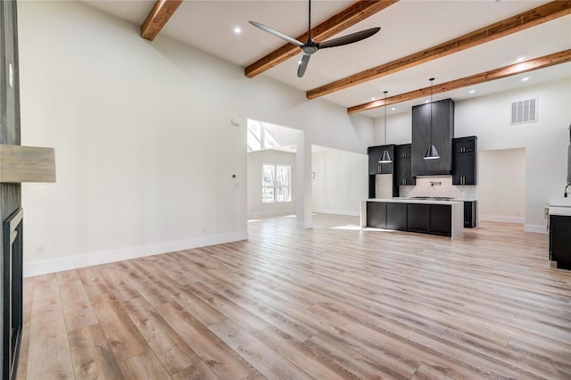 unfurnished living room featuring beam ceiling, ceiling fan, sink, light hardwood / wood-style floors, and a fireplace