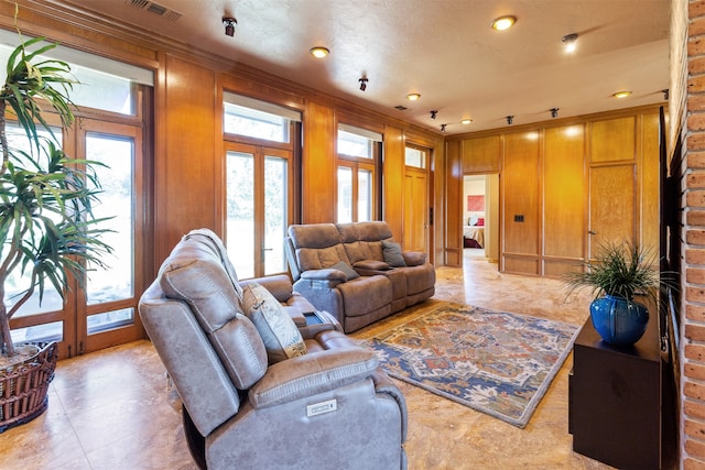 living room with french doors, crown molding, a textured ceiling, and wood walls