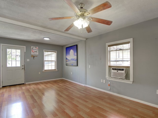 empty room with a wealth of natural light, cooling unit, a textured ceiling, and light hardwood / wood-style floors