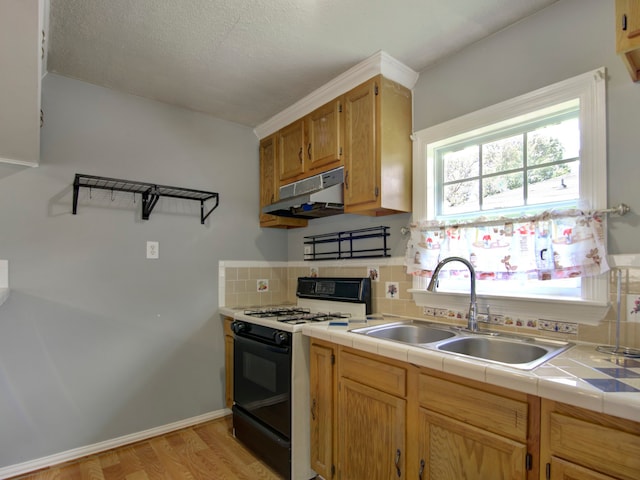 kitchen with tasteful backsplash, sink, gas stove, light hardwood / wood-style floors, and tile counters