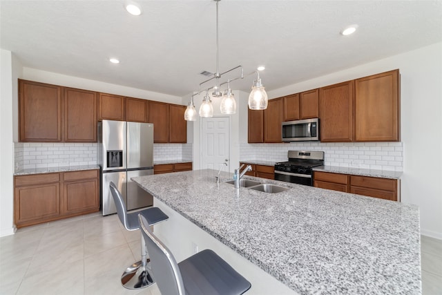 kitchen featuring a breakfast bar area, stainless steel appliances, sink, decorative light fixtures, and light stone counters