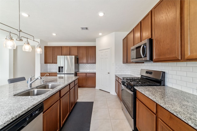 kitchen featuring hanging light fixtures, sink, light stone counters, and stainless steel appliances