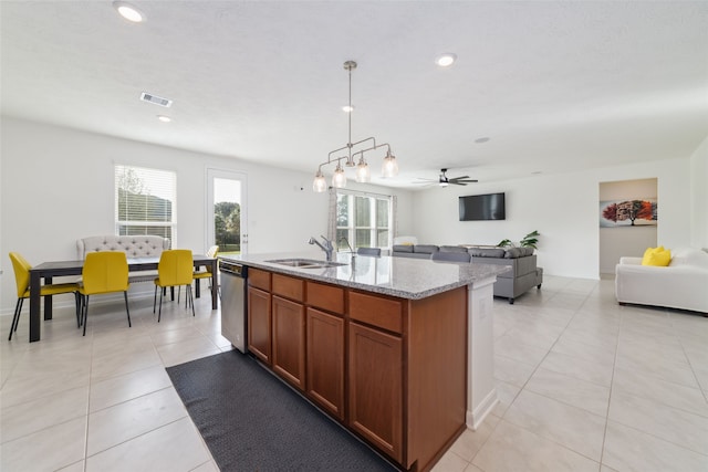 kitchen featuring a center island with sink, sink, decorative light fixtures, stainless steel dishwasher, and light stone counters