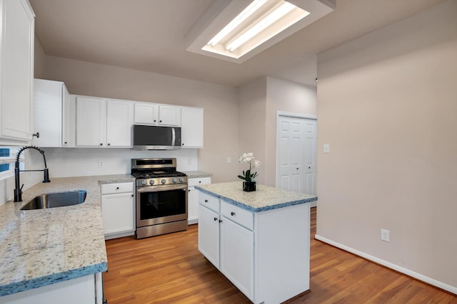 kitchen featuring white cabinets, sink, light stone countertops, appliances with stainless steel finishes, and a kitchen island