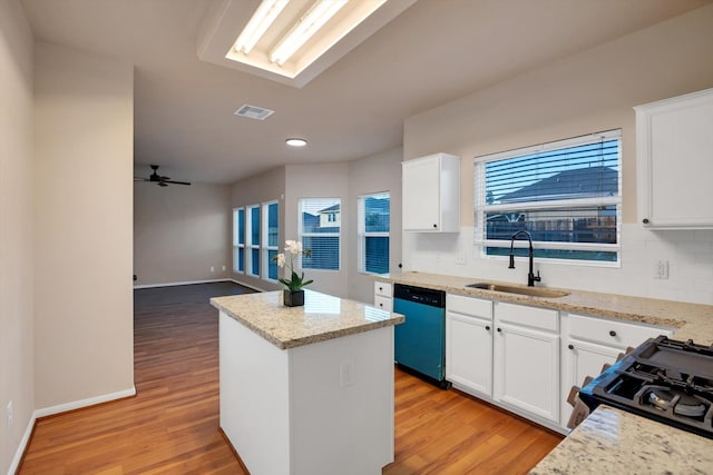 kitchen with light stone countertops, dishwasher, sink, a kitchen island, and white cabinets