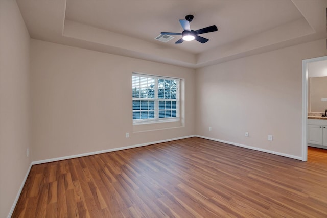 empty room with hardwood / wood-style floors, a tray ceiling, and ceiling fan