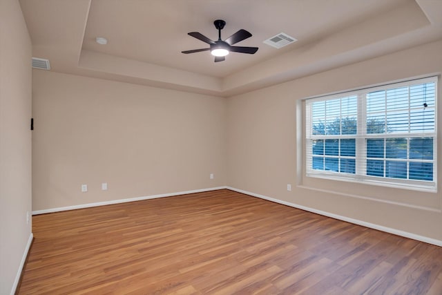 spare room with a raised ceiling, ceiling fan, and light hardwood / wood-style floors