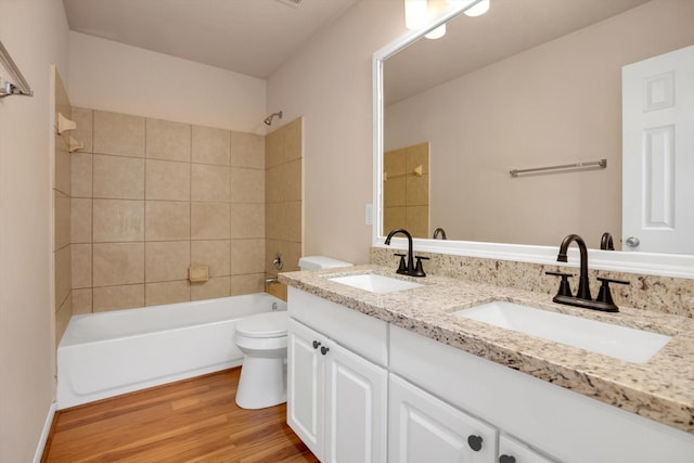 full bathroom featuring vanity, hardwood / wood-style floors, tiled shower / bath combo, and toilet