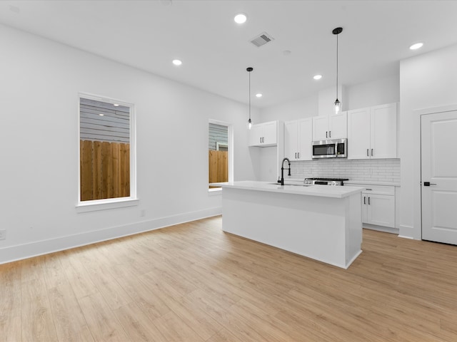 kitchen featuring a kitchen island with sink, hanging light fixtures, white cabinets, light wood-type flooring, and appliances with stainless steel finishes