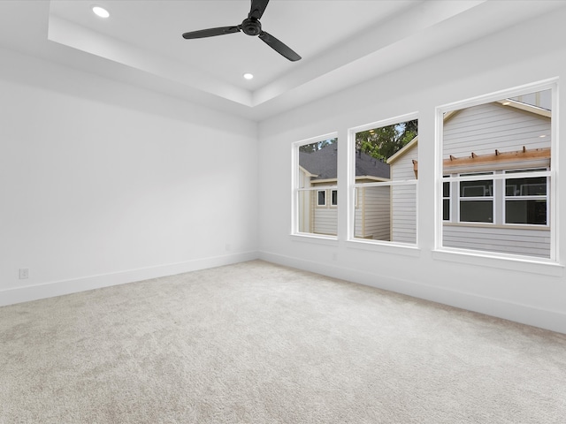 empty room featuring ceiling fan, a raised ceiling, and carpet