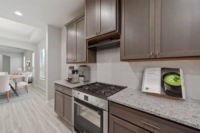 kitchen with light stone countertops, decorative backsplash, light hardwood / wood-style flooring, and high end range