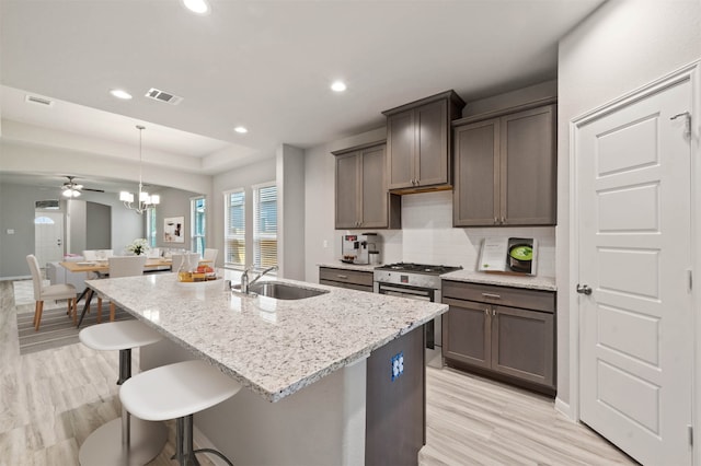 kitchen featuring gas range, a center island with sink, sink, light stone countertops, and light wood-type flooring