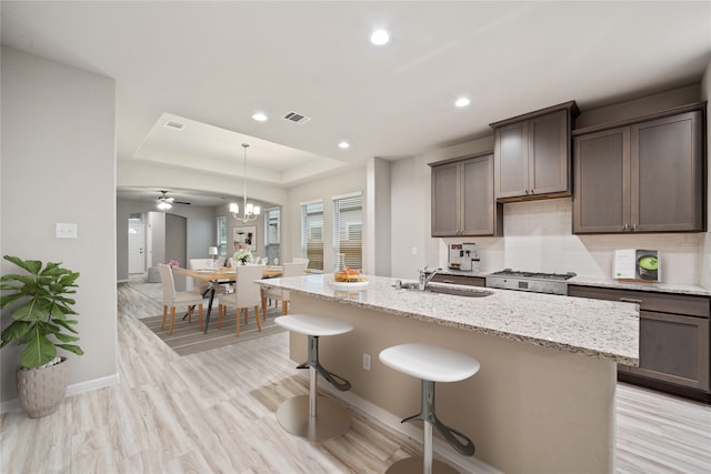 kitchen featuring sink, a kitchen bar, an island with sink, light wood-type flooring, and backsplash