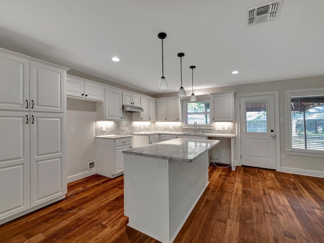 kitchen with light stone countertops, a center island, white cabinets, and dark wood-type flooring