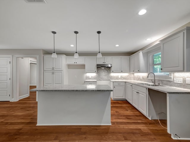 kitchen featuring dark wood-type flooring, a center island, decorative light fixtures, and white cabinetry