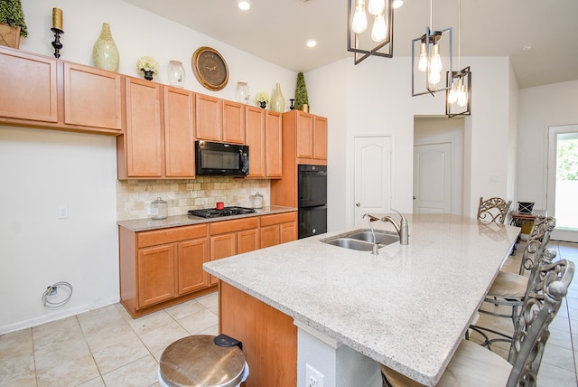 kitchen featuring hanging light fixtures, an island with sink, black appliances, sink, and light stone counters