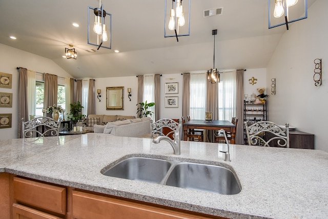 kitchen featuring lofted ceiling, light stone counters, sink, and pendant lighting