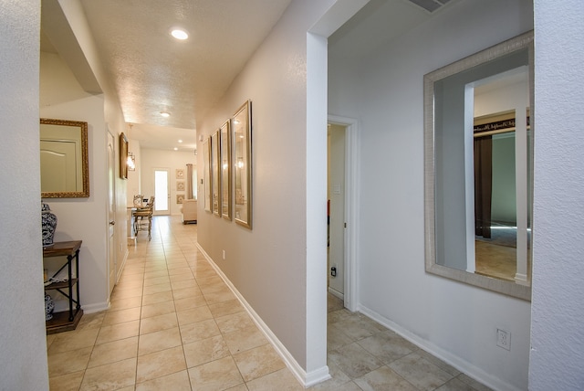 hall with a textured ceiling and light tile patterned floors