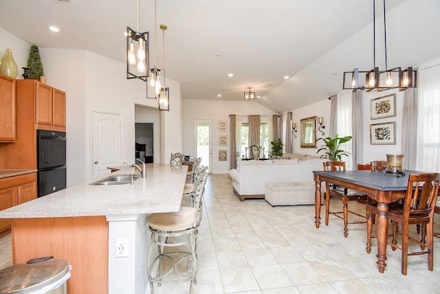 kitchen featuring lofted ceiling, double oven, a kitchen island with sink, sink, and decorative light fixtures