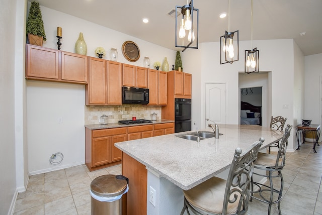 kitchen with light stone counters, a kitchen island with sink, black appliances, sink, and decorative light fixtures