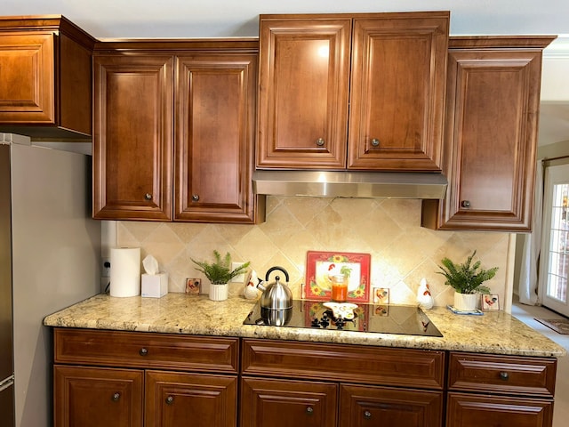 kitchen featuring light stone counters, black electric cooktop, backsplash, and stainless steel refrigerator