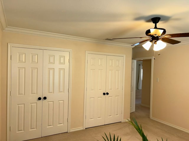 unfurnished bedroom featuring light carpet, two closets, ceiling fan, and ornamental molding