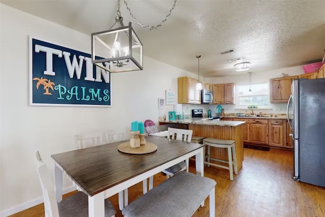 dining area with a textured ceiling, sink, light wood-type flooring, and a notable chandelier