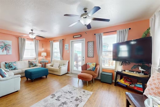 living room featuring a wealth of natural light, ceiling fan, a textured ceiling, and light hardwood / wood-style flooring