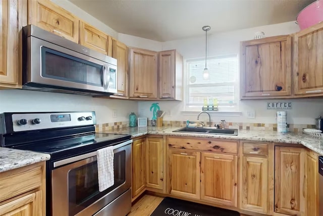 kitchen with light stone counters, appliances with stainless steel finishes, pendant lighting, sink, and light hardwood / wood-style floors