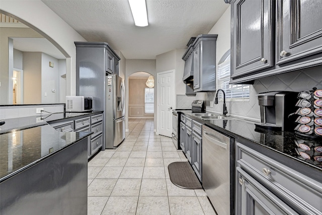 kitchen with sink, appliances with stainless steel finishes, backsplash, and dark stone counters