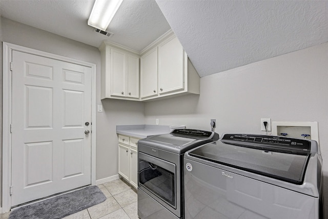 laundry room with light tile patterned floors, a textured ceiling, separate washer and dryer, and cabinets