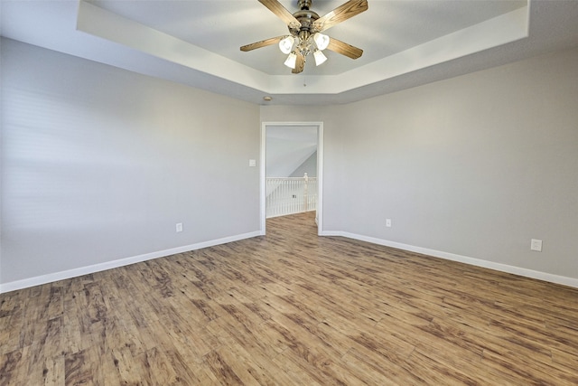 empty room with ceiling fan, a raised ceiling, and wood-type flooring