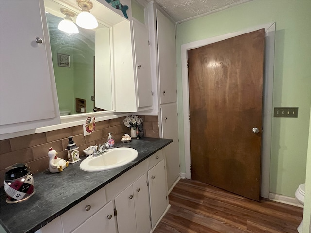 bathroom featuring hardwood / wood-style floors, vanity, toilet, a textured ceiling, and tasteful backsplash